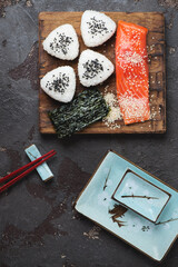 Japanese onigiri, slice of salmon fillet and nori on a rustic wooden chopping board, flat lay on a brown stone background, vertical shot