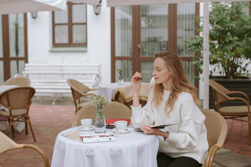 Beautiful young woman sitting in city cafe, having breakfast and making sketches. Artist, education, occupation concept.