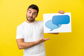 Young handsome caucasian man isolated on yellow background holding a placard with speech bubble icon and pointing it