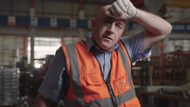 Close up, male engineer caucasian at an industrial factory takes off his hat to wipe away the sweat on his face.