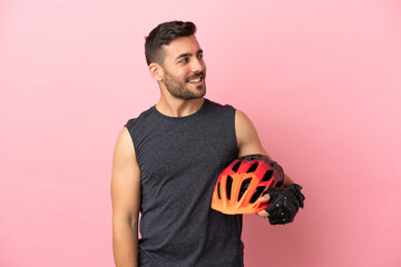 Young cyclist man isolated on pink background looking to the side and smiling - obrazy, fototapety, plakaty