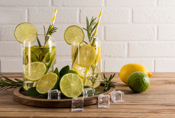 two glasses of refreshing citrus water, a cocktail or tonic with ice cubes on a wooden table against a white brick wall. useful detox.