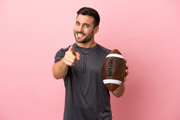 Young caucasian man playing rugby isolated on pink background pointing front with happy expression