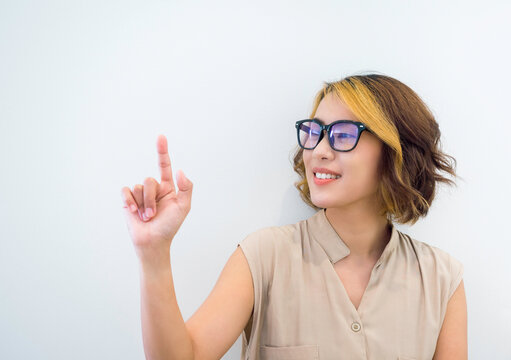 Happy smile Asian woman short hair wearing eyeglasses with blue filter touch on virtual touch screen by finger on white background. Hand point or press on empty space by businesswoman's hand.