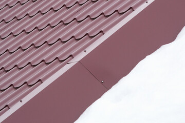 Snow and details of the structure of the roof made of brown metal tiles.