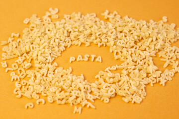 Whole grain dark pasta letters on dark yellow textured background with selected focus