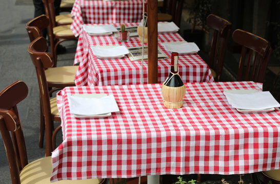 tables of an outdoor restaurant with red and white checkered tablecloths is a flask of good wine