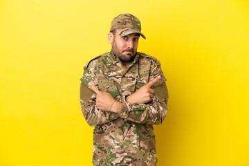 Military man isolated on yellow background pointing to the laterals having doubts