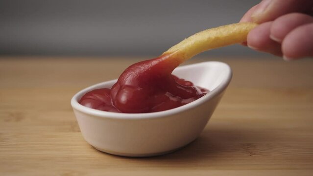 Mixing tomato ketchup sauce with french fries on a wooden background. Closeup view. Junk food concept