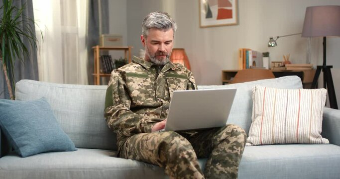 Caucasian man in military clothes using laptop at home