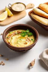 A bowl of hummus or fava and a tray of hot pita. Close-up on a light wooden background
