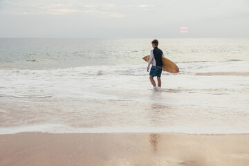 A handsome teenage boy with a surfboard going into the ocean on a sandy beach on the surf line of Sri Lanka.