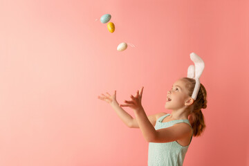 Beautiful cute little girl in Easter bunny ears with colorful easter eggs on a pink background. Easter postcard