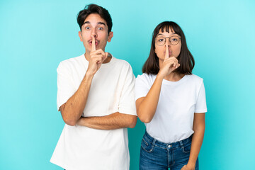 Young mixed race couple isolated on blue background showing a sign of silence gesture putting finger in mouth