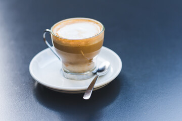 Creamy coffee in a glass cup on a dark table.