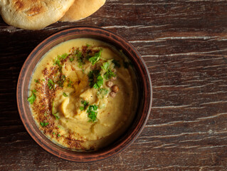 Hummus or vegetable paste in a bowl, top view on a wooden background with pita bread. Close-up, copy of the space.