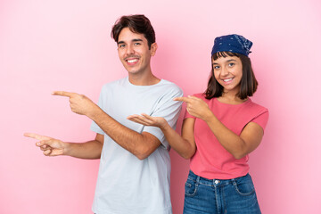 Young couple isolated on pink background extending hands to the side for inviting to come