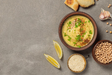 Chickpea or pea paste in a brown bowl. On a gray background, with pita bread and cooking ingredients.