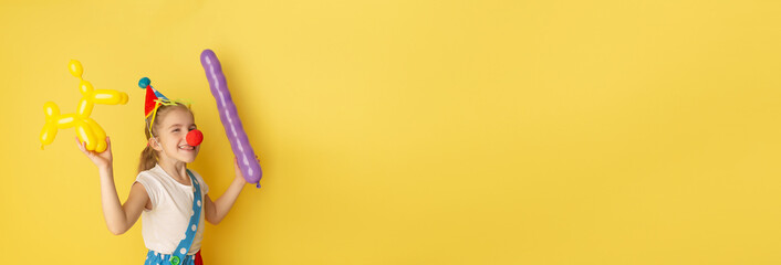 Banner. Funny kid clown against yellow background. Happy child playing with festive decor. Birthday and 1 April Fool's day concept