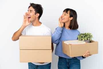 Young couple making a move while picking up a box full of things isolated on white background shouting with mouth wide open to the lateral