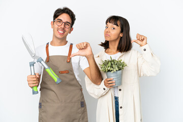 Young mixed race gardeners holding a plant and pruning shears isolated on white background proud and self-satisfied in love yourself concept