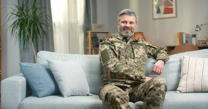 Mature army soldier sitting on sofa and smiling on camera