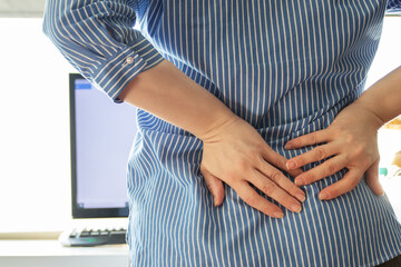 Osteochondrosis, backache, a woman in the office in a chair holds her back with her hand, the spine...