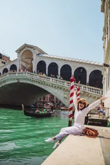 Tuinposter woman sitting near rialto bridge in venice italy looking at grand canal with gondolas © phpetrunina14