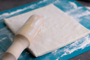 A piece of puff pastry and a wooden rolling pin on a turquoise board