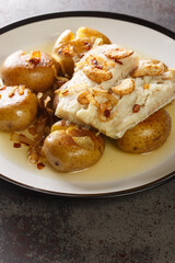 Bacalhau a Lagareiro Grilled Salted Cod with Olive Oil served with baked Potatoes closeup in the plate on the table. Vertical