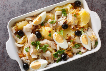 Portuguese Bacalhau a Gomes de Sa salted cod baked with potatoes, onions served with eggs and olives close-up in a baking dish on the table. horizontal top view from above - obrazy, fototapety, plakaty