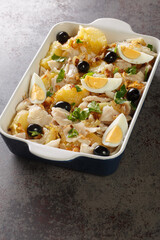 Bacalhau a Gomes de Sa cod fish with potatoes, onion, olives, eggs and garlic closeup in the baking dish on the table. Vertical