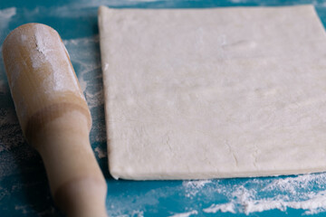A piece of puff pastry and a wooden rolling pin on a turquoise board