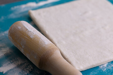 A piece of puff pastry and a wooden rolling pin on a turquoise board