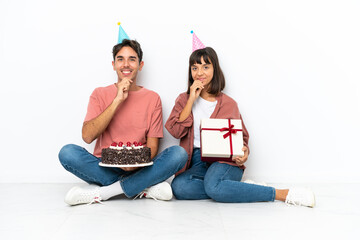 Young mixed race couple celebrating a birthday sitting on the floor isolated on white background smiling with a sweet expression