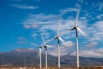 group of windmills in line, with the blades in motion. blue sky with clouds