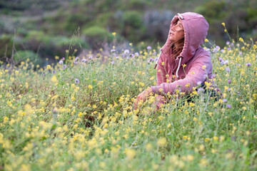 woman looking at the sky at dawn green and flowery meadow in spring, pink sweater with hoodie