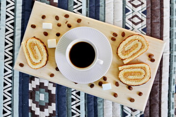 morning breakfast - cup of strong invigorating black coffee between coffee beans with fresh sweet pastries and sugar cubes on a wooden board. top view, flat lay