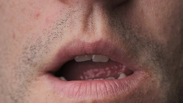Man erotically licks his lips close-up. Close-up portrait of the face of a young man with stubble who is sexually licking his lips with his tongue. Macro of seductive young man. Sexually horny concept