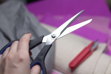 Scissors in hand against the background of different fabrics and tailor's accessories