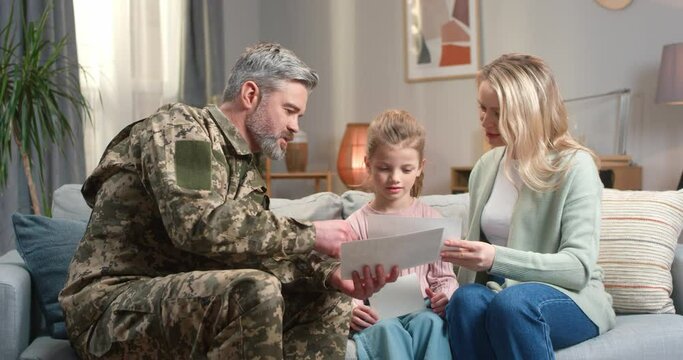 Soldier showing photos to wife and daughter at home