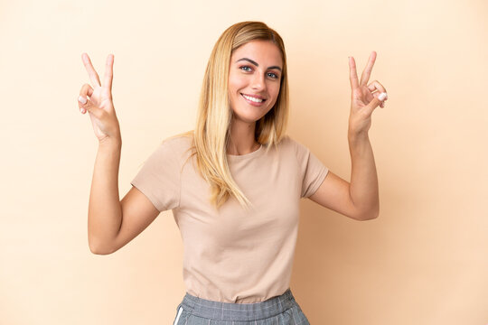 Blonde Uruguayan girl isolated on beige background showing victory sign with both hands