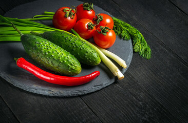 Menu idea with space for hotel recipe. Fresh vegetable salad set. Red tomatoes and green young onions with cucumber on a black plate