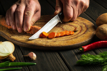 The cook cutting carrots for vegetable soup in a kitchen table. Close-up of the hands of the chef during work. Vegetarian cuisine