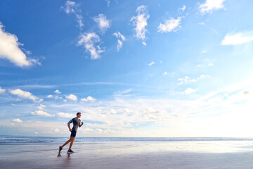 Fototapeta na wymiar Enjoying sports lifestyle. Happy young man in headphones jogging on the sea shore.