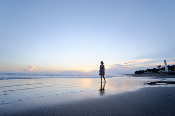 Sky and sea. Beautiful sunset. Silhouette of young woman walking on ocean beach.