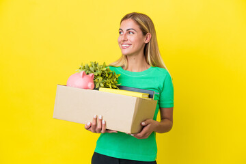Young Uruguayan girl making a move while picking up a box full of things isolated on yellow...