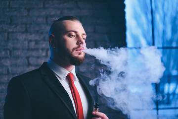 Elegant vaper. Handsome young bearded man in suit smoking vaporizer electronic cigarette.