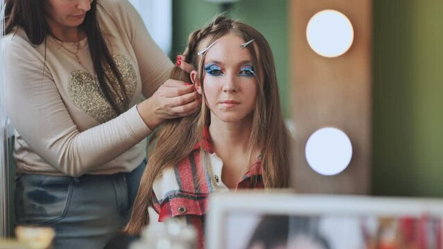 The girl makeup artist makes a braid for the model.