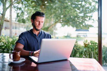 Freelance concept. Young  bearded man using laptop while sitting on summer terrace.